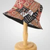 Reversible bucket hat with vibrant African-inspired geometric and abstract print in black, orange, brown, and white. Shown on a wooden stand.