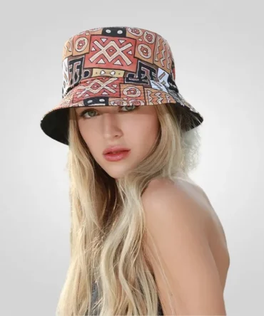 Woman wearing a vibrant African print bucket hat with geometric patterns in orange, black, brown, and white, styled with long blonde hair.