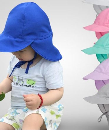 Baby wearing a blue sun hat with a wide brim and neck flap for UV protection. Stack of various colored baby sun hats in the background.