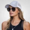 "Woman wearing a light grey and white trucker hat with a tonal American flag design, aviator sunglasses, and a black tank top, showcasing a casual outdoor style."