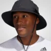 A man wearing a black Adidas Victory 4 bucket hat with a wide brim, drawstring, and Adidas logo. He is also wearing a white Adidas t-shirt.