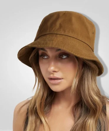 Close-up of a brown canvas bucket hat with a wide brim, featuring a woman with long, wavy brown hair looking to the side. The hat appears to be made of a durable fabric suitable for travel.