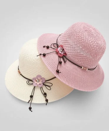 Two foldable beach hats, one white and one pink, featuring floral and beaded accents. Ideal for summer and travel.